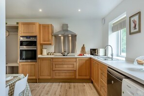 A modern kitchen with wooden cabinets, stainless steel appliances, a window with a view, and a dining area with a checkered tablecloth. - 1 Bed in Beckingham (oc-b42840) (Beckingham)