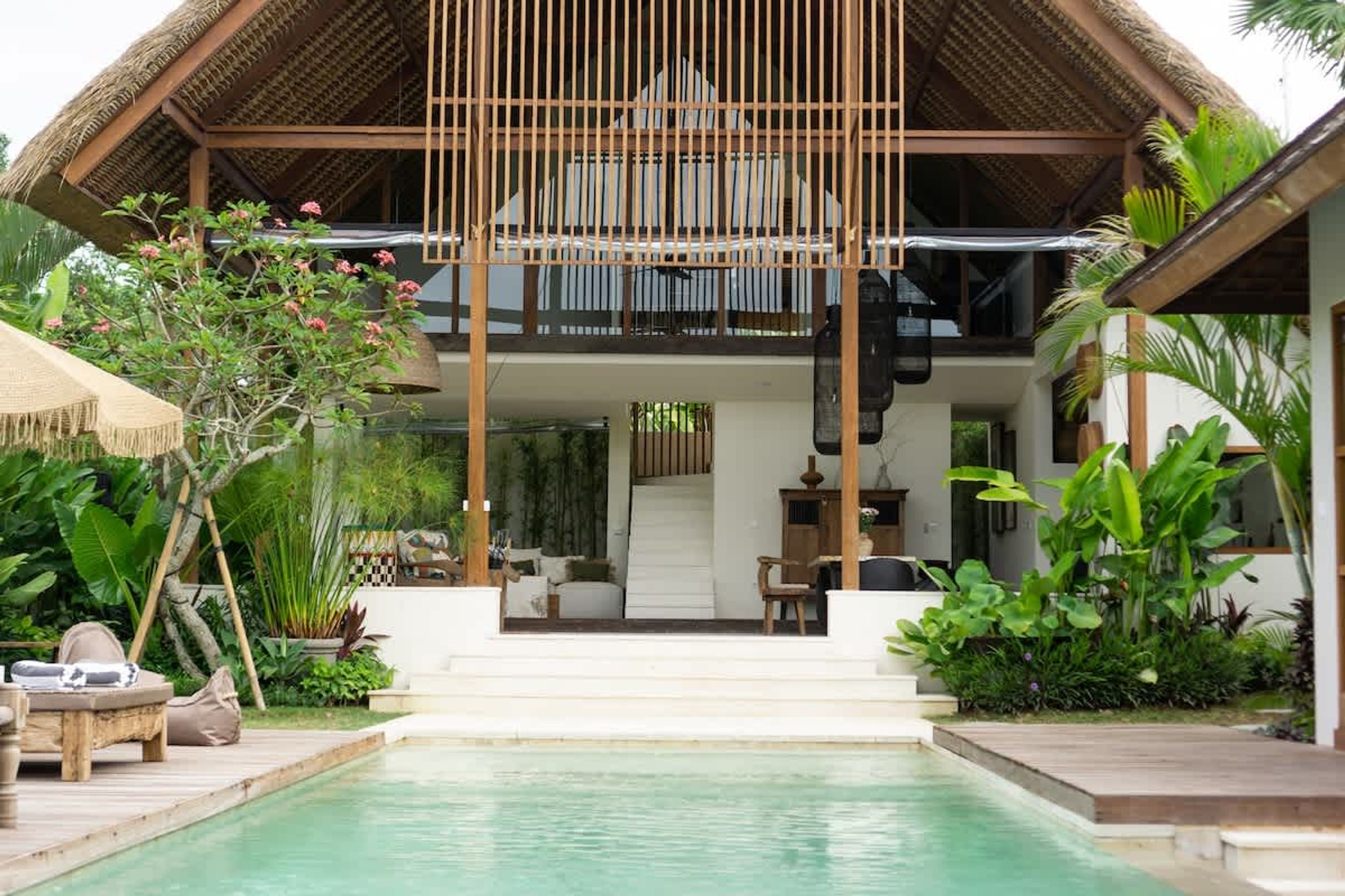 Eine moderne Villa mit Pool, einer überdachten Sitzgelegenheit im Freien und üppigen tropischen Pflanzen.