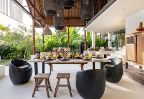 An outdoor dining area with a table set for four, surrounded by black chairs, under a wooden pergola with hanging lights. - Villa Chempaka in Canggu (Canggu)