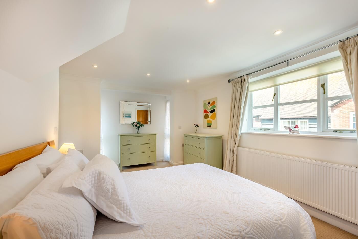 A bedroom with a large bed, a dresser, a mirror, and a window with curtains.