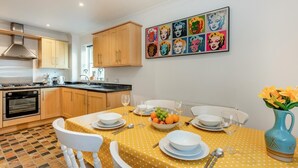 A modern kitchen with wooden cabinets, a dining table set with plates, glasses, and a fruit bowl. - 2 Bed in Rye (oc-f44884) (Rye)