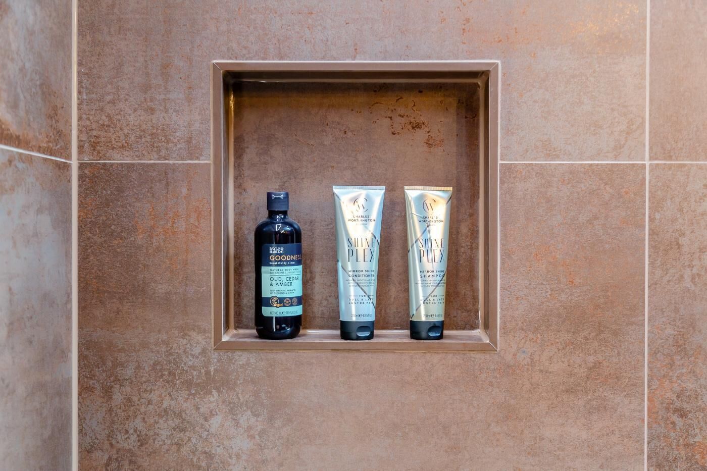 A bathroom with a shelf containing a bottle of body wash and two tubes of shampoo.