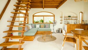 Ein Loft-Zimmer mit einer Holztreppe, einem grünen Sofa, einem Esstisch und einer Küchenzeile.