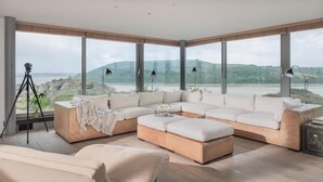 Ein modernes Wohnzimmer mit einer Eckcouch, einer Liege und einem großen Fenster mit Blick auf eine natürliche Landschaft.