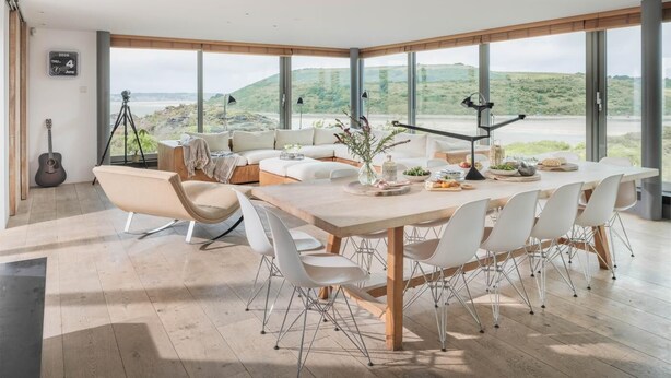 Ein moderner Essbereich mit einem großen Tisch, weißen Stühlen und Blick auf eine grüne Landschaft durch große Fenster.