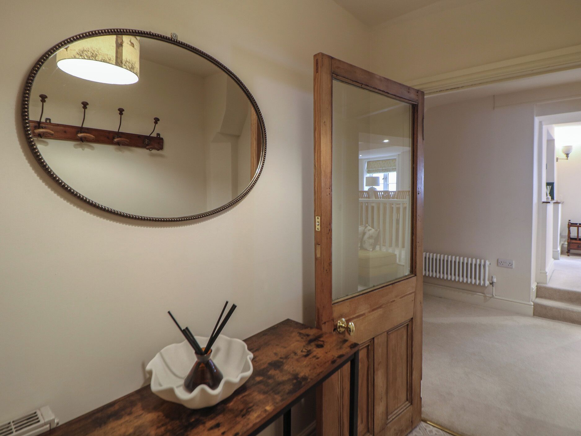 Un baño con tocador de madera, un espejo redondo con detalle de cuentas y un lavabo blanco con dispensador de jabón.