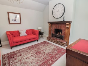 Una sala de estar con un sofá rojo, un tapete estampado, una chimenea y un reloj de pared grande.
