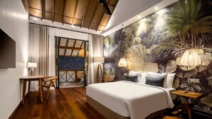 Ein Schlafzimmer mit einem großen Bett, Holzböden, einem Schreibtisch und einer Wandmalerei von tropischen Pflanzen.