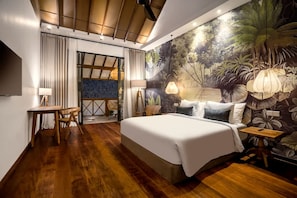 A bedroom with a large bed, wooden flooring, a desk, and a mural of tropical foliage. - Nusantara Loft Ndao in Pererenan (Pererenan)