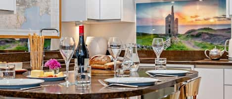 Un comedor con una mesa redonda preparada para dos personas, una botella de vino, copas, una jarrón y una tetera.