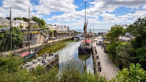 En havn med fortøjede både, en stenvæg og bygninger langs vandet.