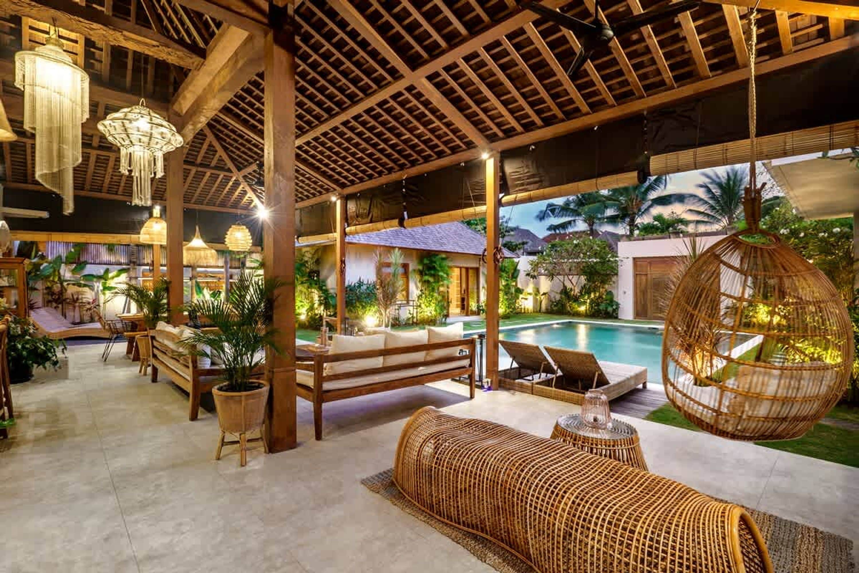 An indoor lounge area with wooden furniture, a pool, and hanging rattan chairs.