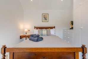 Ein Schlafzimmer mit einem hölzernen Bett, einem Nachttisch mit Lampe, einer Kommode und einem gerahmten Bild an der Wand.
