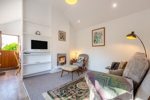 Ein modernes Wohnzimmer mit Kamin, einem an der weißen Wand befestigten Fernseher, einer gemütlichen Couch und einem gemusterten Teppich.