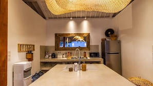 A modern kitchen with a central island, a large woven light fixture, a refrigerator, and a microwave. - Villa M2 in Seminyak (Seminyak)