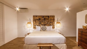A bedroom with a large bed, a wooden headboard with shelves, two wall-mounted lamps, a small wooden table, and a dresser with drawers. - Villa M2 in Seminyak (Seminyak)