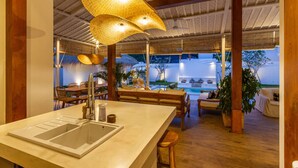 A spacious indoor area with a large island counter, wooden furniture, and a view of an outdoor pool area. - Villa M2 in Seminyak (Seminyak)