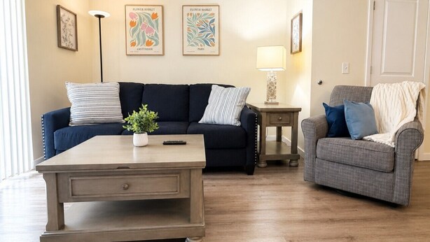 A living room with a dark blue sofa, a grey armchair, a wooden coffee table, and a small side table with a lamp.