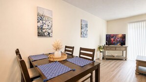 A dining area with a wooden table, four chairs, blue placemats, and two wall-mounted paintings.