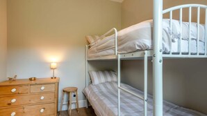 Ein Schlafraum mit Etagenbetten, einem Holzschrank und einem kleinen Hocker.