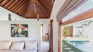 Ein Schlafzimmer mit einem Bett, einem Gemälde, einer Decke mit Holzstruktur und Blick auf einen Swimmingpool.