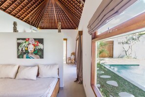 A bedroom with a bed, a painting, a ceiling with a wooden pattern, and a view of a swimming pool. - Villa Namu in Seminyak (Seminyak)