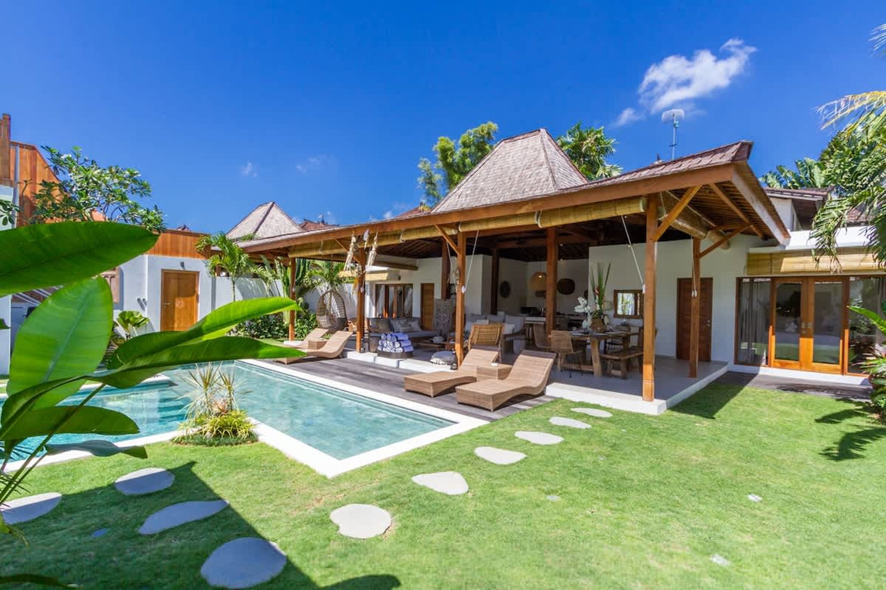 A poolside area with lounge chairs, a covered seating area, and a clear blue sky.