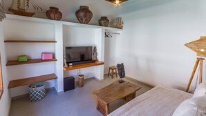 Ein modernes Wohnzimmer mit Fernseher, Holzregalen, einem kleinen Hocker und einer gewebten Lampe.