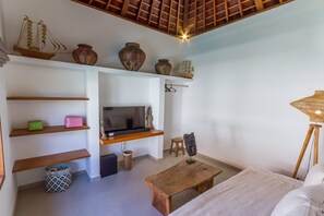 A modern living room with a TV, wooden shelves, a small stool, and a woven lamp. - Villa Namu in Seminyak (Seminyak)
