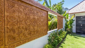 Eine Wand mit filigranen floralen Schnitzereien, einem gepflegten Rasen und einem Gebäude mit einem Ziegeldach.