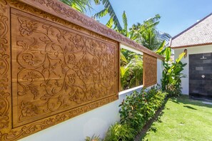 A wall with intricate floral carvings, a well-maintained lawn, and a building with a tiled roof. - Villa Namu in Seminyak (Seminyak)