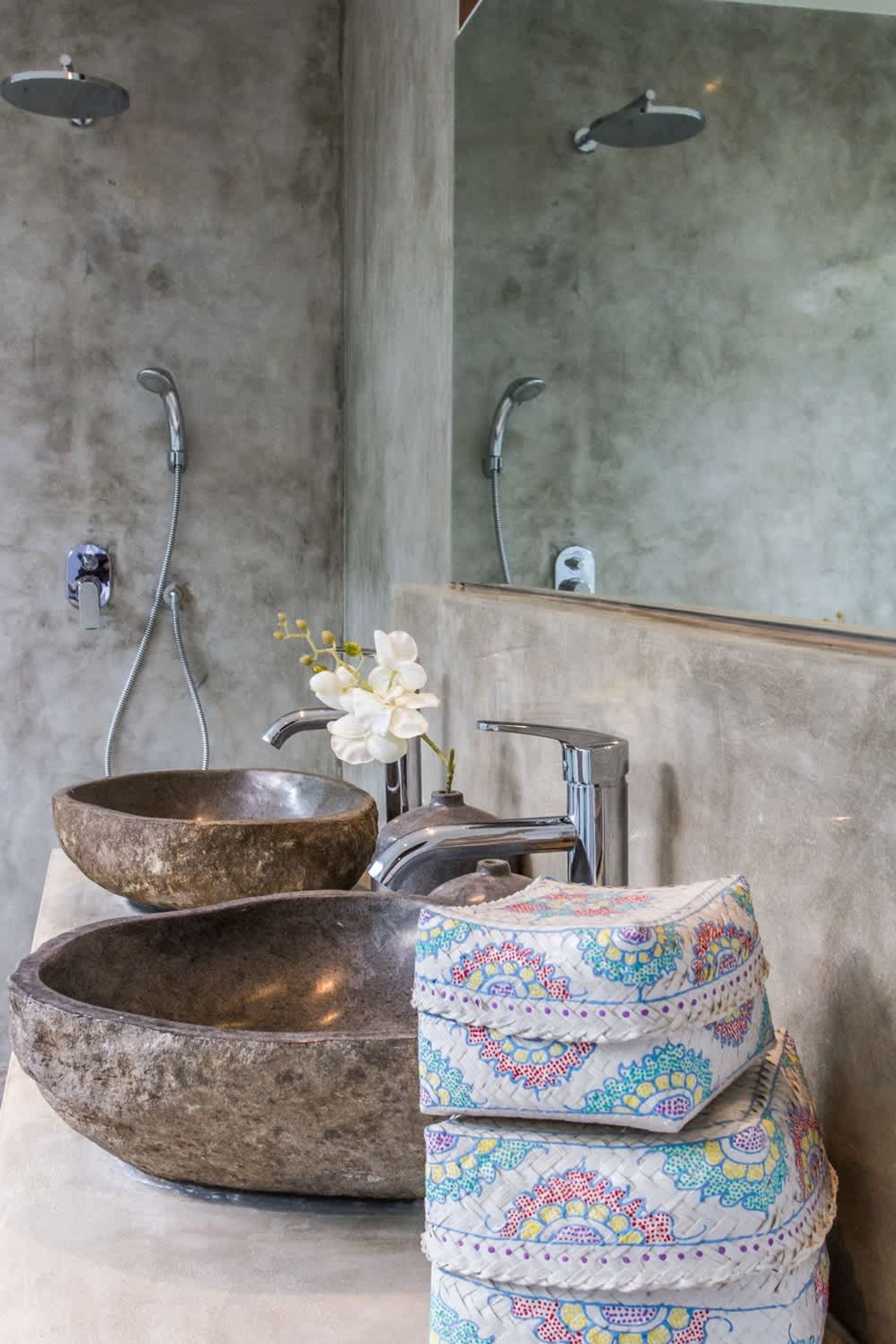 Een badkamer met een grote, rustieke stenen wasbak, een moderne kraan, een handdouche en een spiegel.