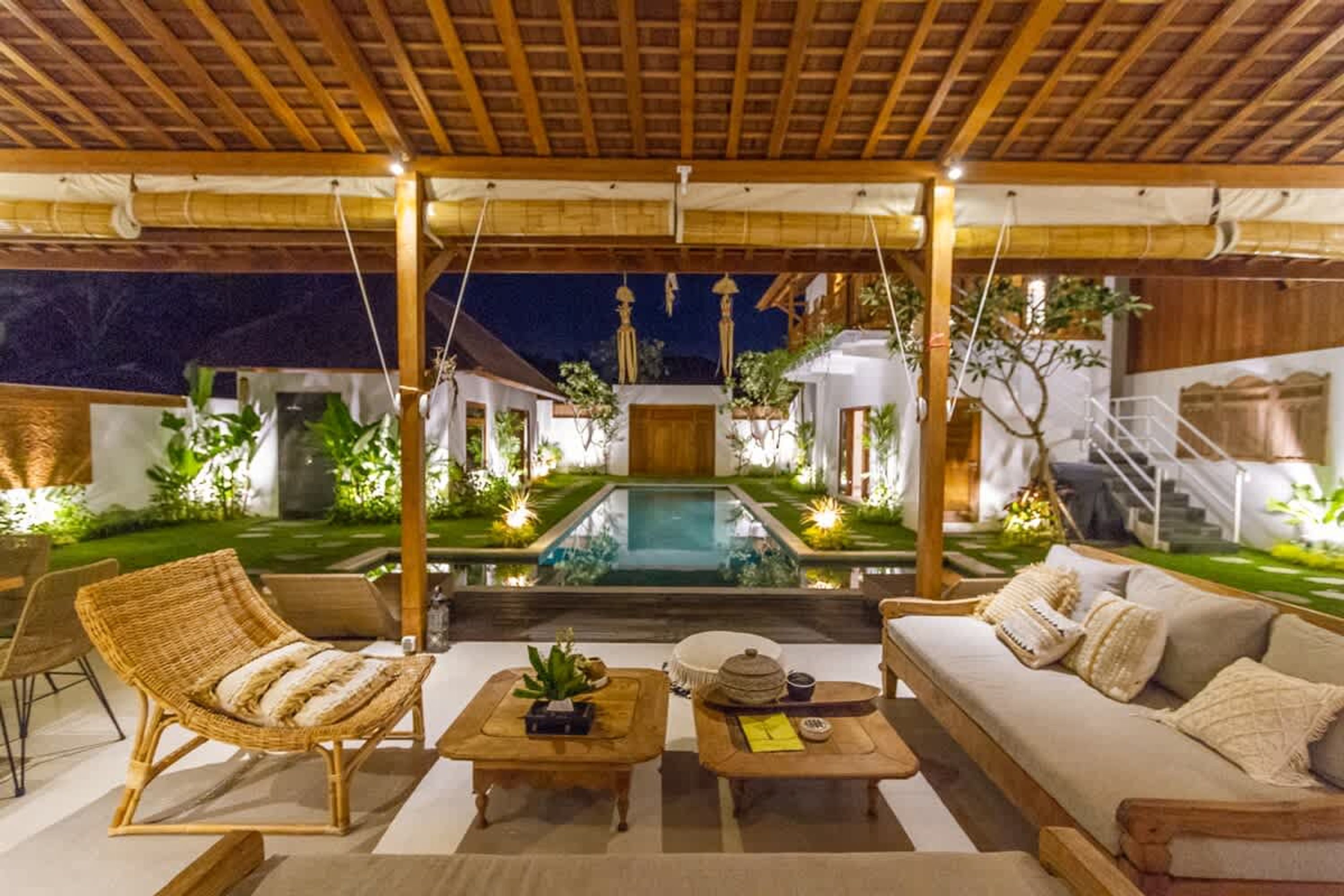 A poolside area with a wooden pergola, lounge chairs, a sofa, and a small table with decorative items.