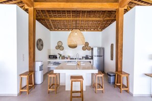 A modern kitchen with a central island, wooden stools, a hanging light fixture, and a wooden ceiling structure. - Villa Namu in Seminyak (Seminyak)
