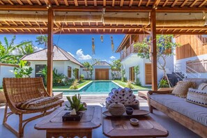 A covered outdoor area with a pool, wicker furniture, and a wooden bench. - Villa Namu in Seminyak (Seminyak)
