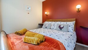 Een net opgemaakt bed met een beddegoed met dessin, twee opgerolde handdoeken en een nachtkastje met een lamp.