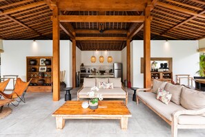 A spacious living area with a wooden ceiling, a sofa, a coffee table, and a bookshelf. - Villa Hana in Seminyak (Seminyak)