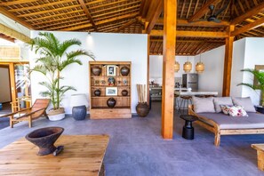 A spacious living area with a wooden ceiling, a sofa, a dining table, and a kitchen in the background. - Villa Hana in Seminyak (Seminyak)