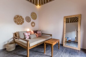 Ein Zimmer mit einer Holzsofa, einem kleinen Holztisch, einem gewebten Korb und einem großen Spiegel.