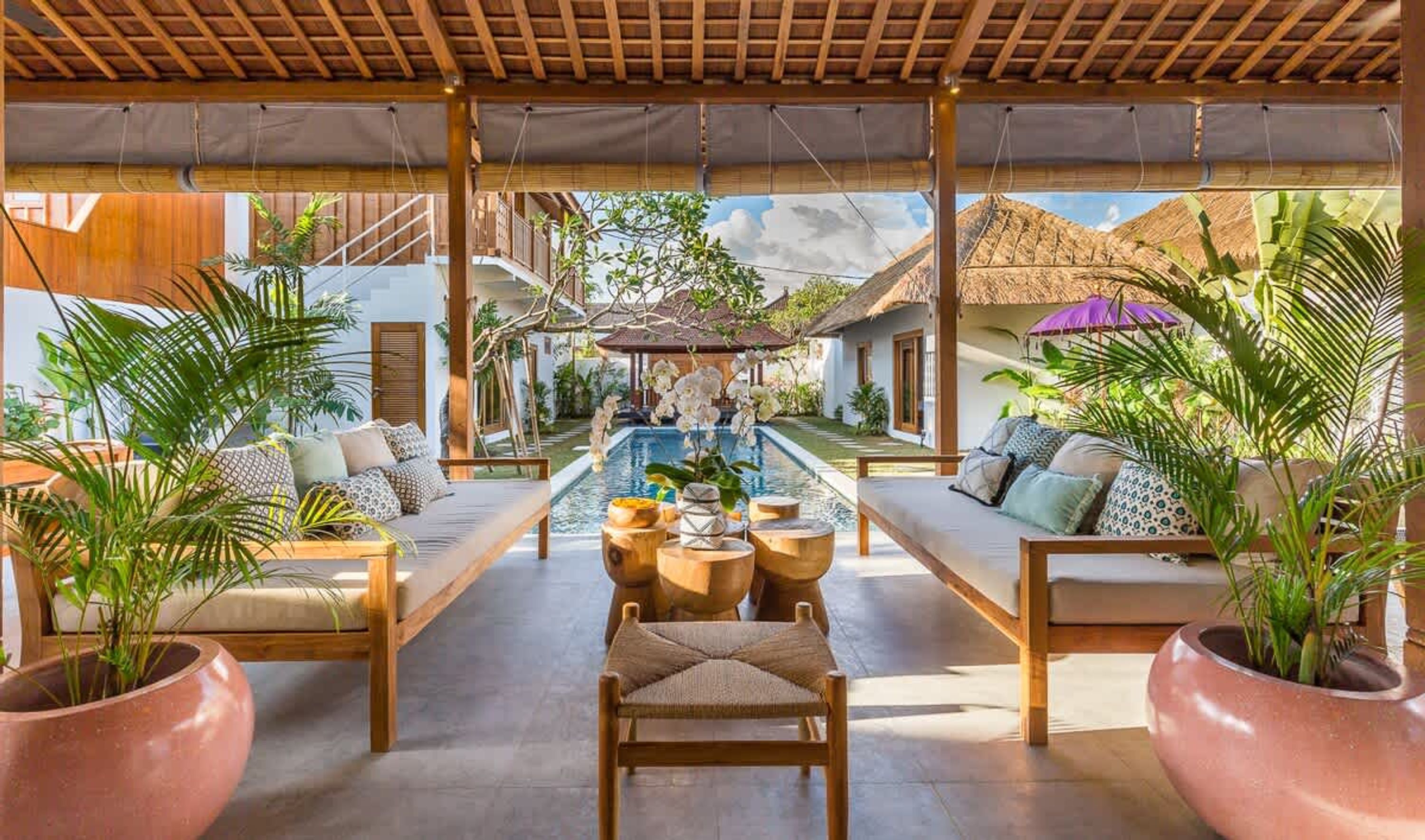 A covered outdoor seating area with a pool, wooden furniture, and potted plants.
