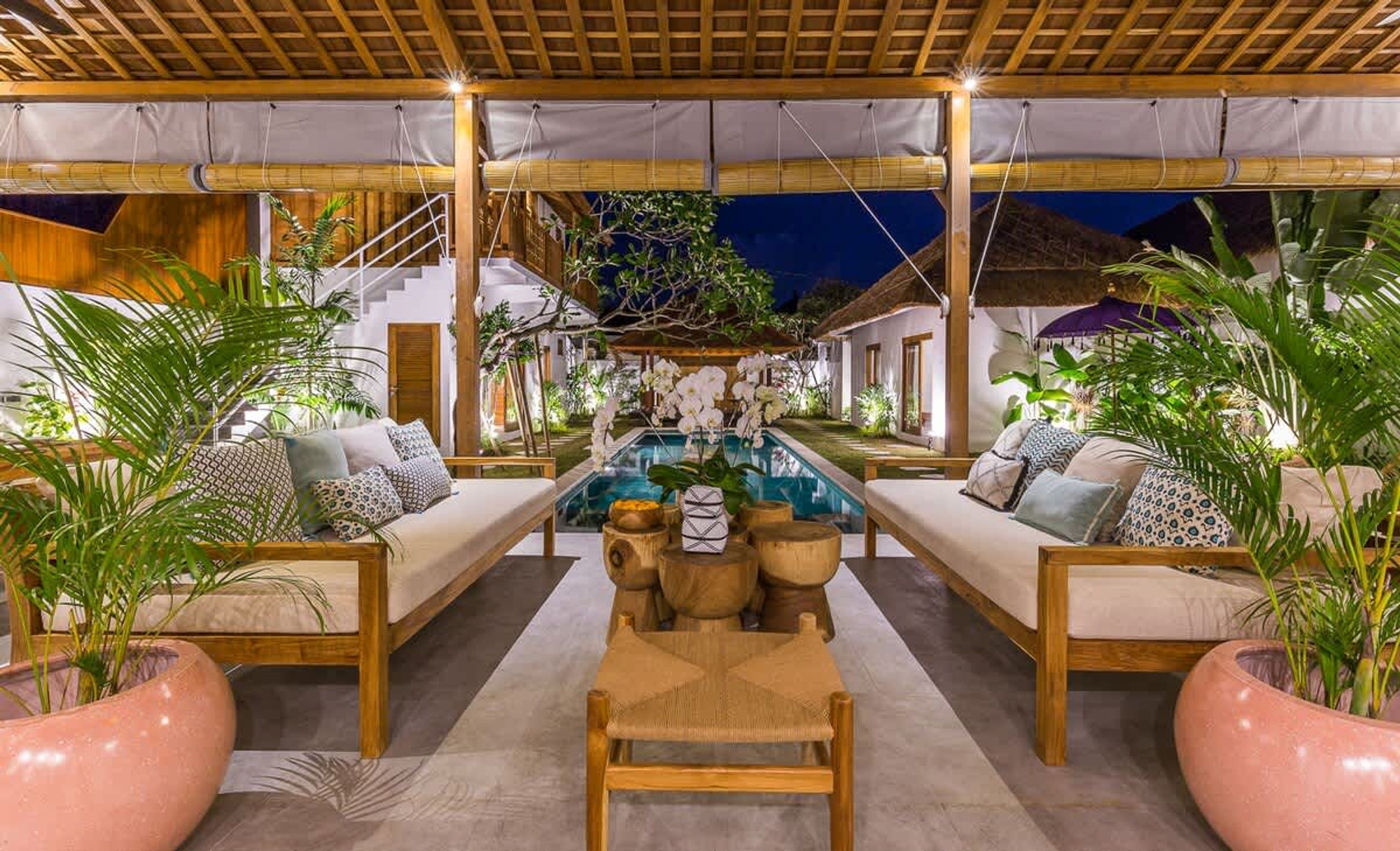 A covered outdoor seating area with a pool, wooden furniture, and potted plants.