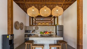 Una cocina con una isla central, taburetes de madera, un refrigerador y lámparas colgantes de mimbre.