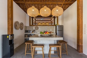 A kitchen with a central island, wooden stools, a refrigerator, and hanging wicker light fixtures. - Villa Hoi in Seminyak (Seminyak)