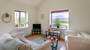 Una camera accogliente con televisione, un tavolino con degli snack, due finestre con tende e vista sul verde.