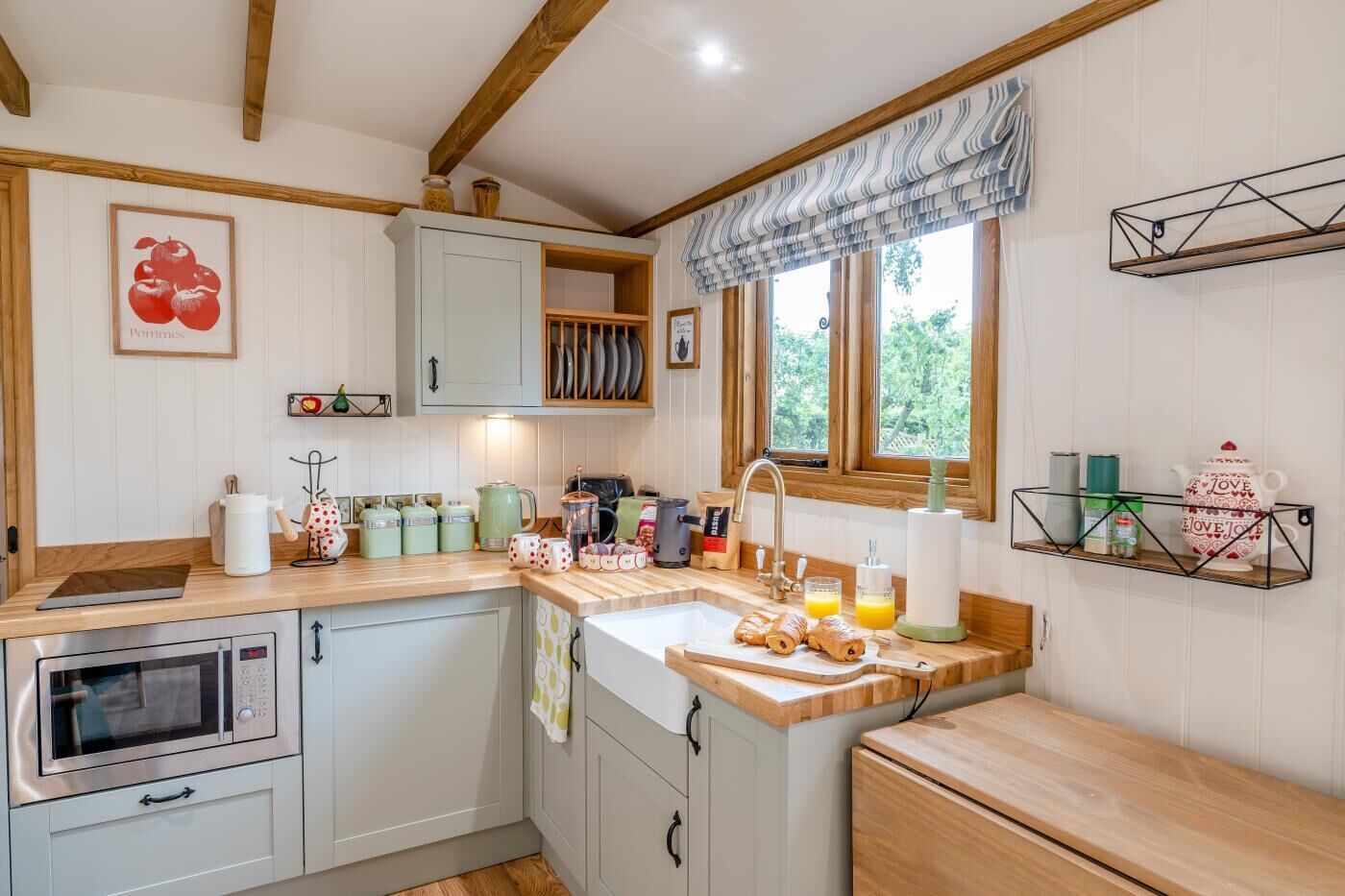 A kitchen with a wooden countertop, a sink, a window with curtains, and a shelf with kitchen items.