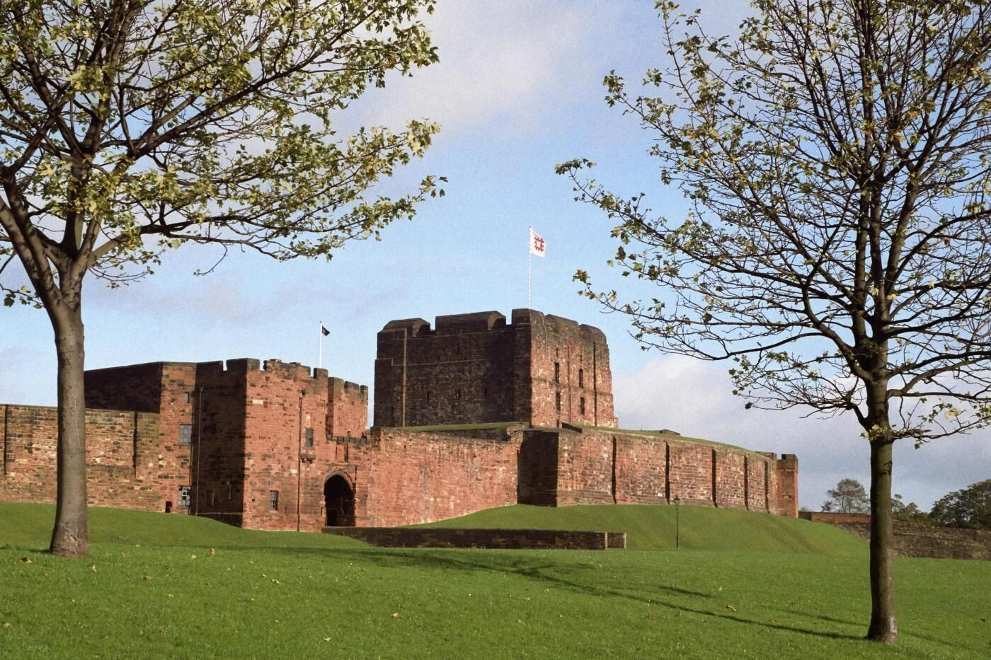 Eine historische Ziegelburg mit Wimpel, umgeben von einer grünen Wiese und Bäumen.