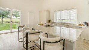 Una cocina moderna con una isla grande, taburetes de bar, un lavamanos y vistas al exterior.