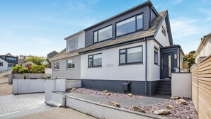 Une maison à deux étages, dotée d’un toit plat, de grandes fenêtres et d’un petit jardin à l’avant.