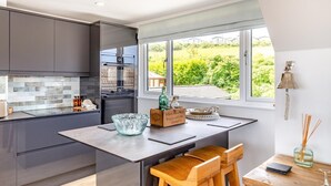 Une cuisine moderne avec des meubles de couleur sombre, un four encastré et une grande fenêtre donnant sur un paysage verdoyant.