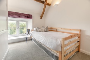A bedroom with a wooden bed, a window with a view of greenery, and a small bedside table with a lamp. - 2 Bed in Swimbridge (oc-p44771) (Swimbridge)